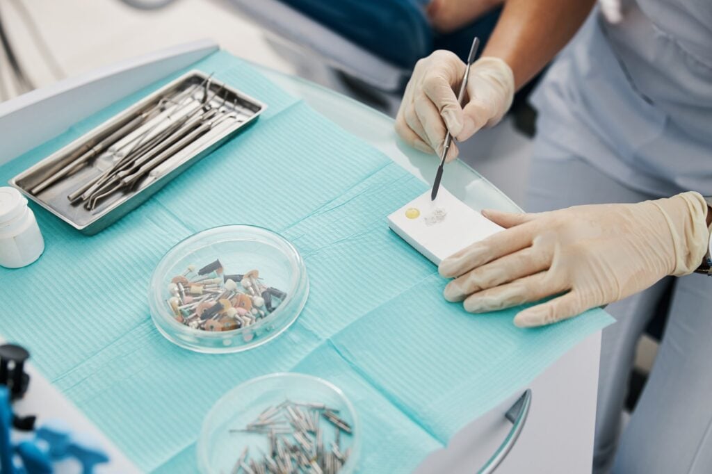 Gloved hands working with dental filling material beside a tray of dental instruments